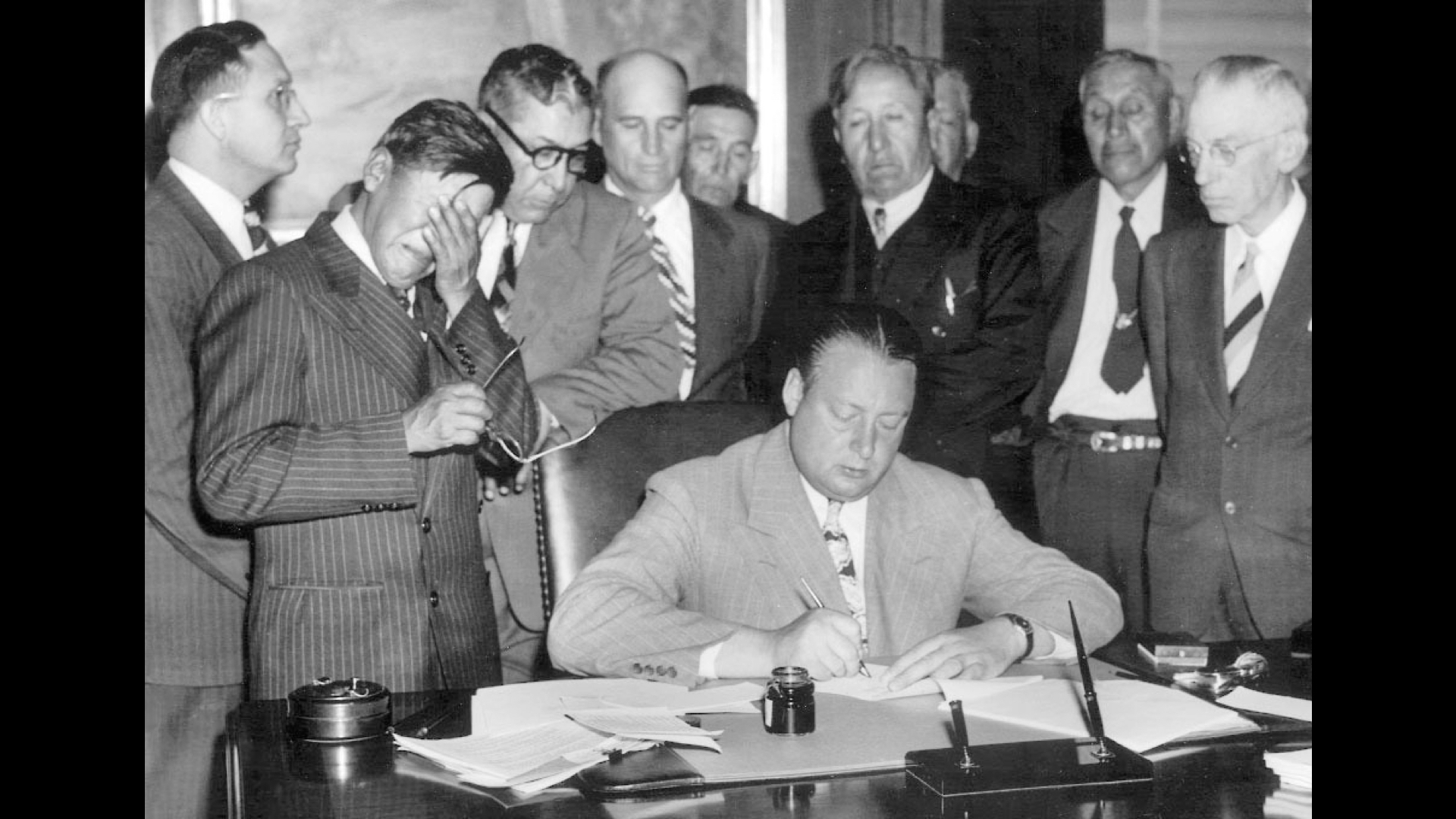 U.S. officials and representatives of the Three Affiliated Tribes (Hidatsa, Mandan, and Arikara) sign the Garrison Dam agreement on May 20, 1948. Secretary of the Interior Julius Krug writing his name while tribal chairman George Gillette sobs into his hand.
